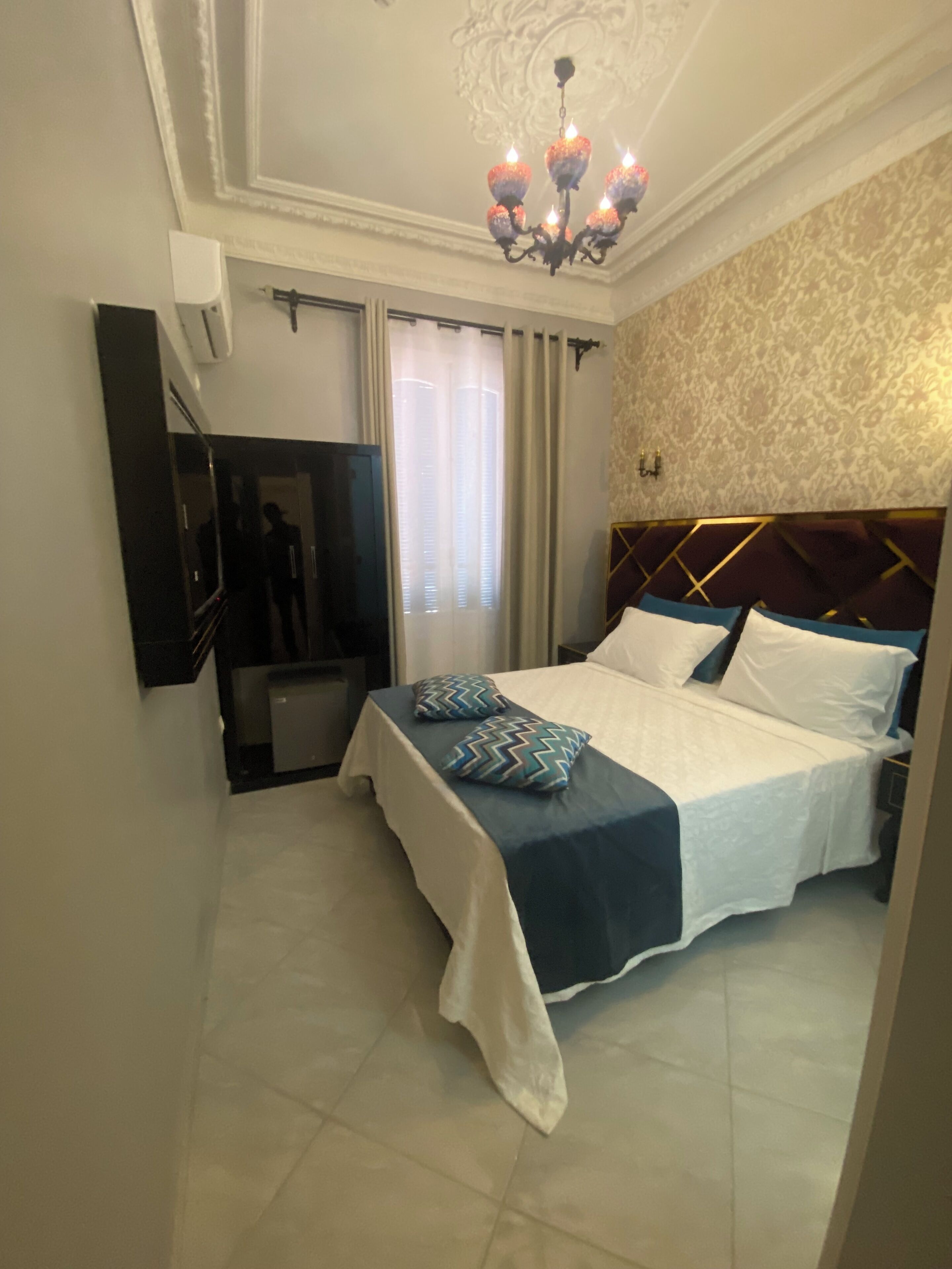 Une chambre d’hôtel avec un lit, une télévision, un lustre et un mur orné de motifs.