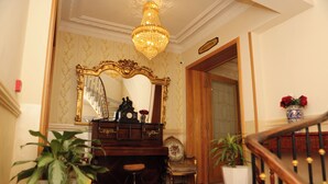 A grand reception area with a chandelier, a large mirror, a piano, and a staircase. - Hotel de letoile (Béjaïa)