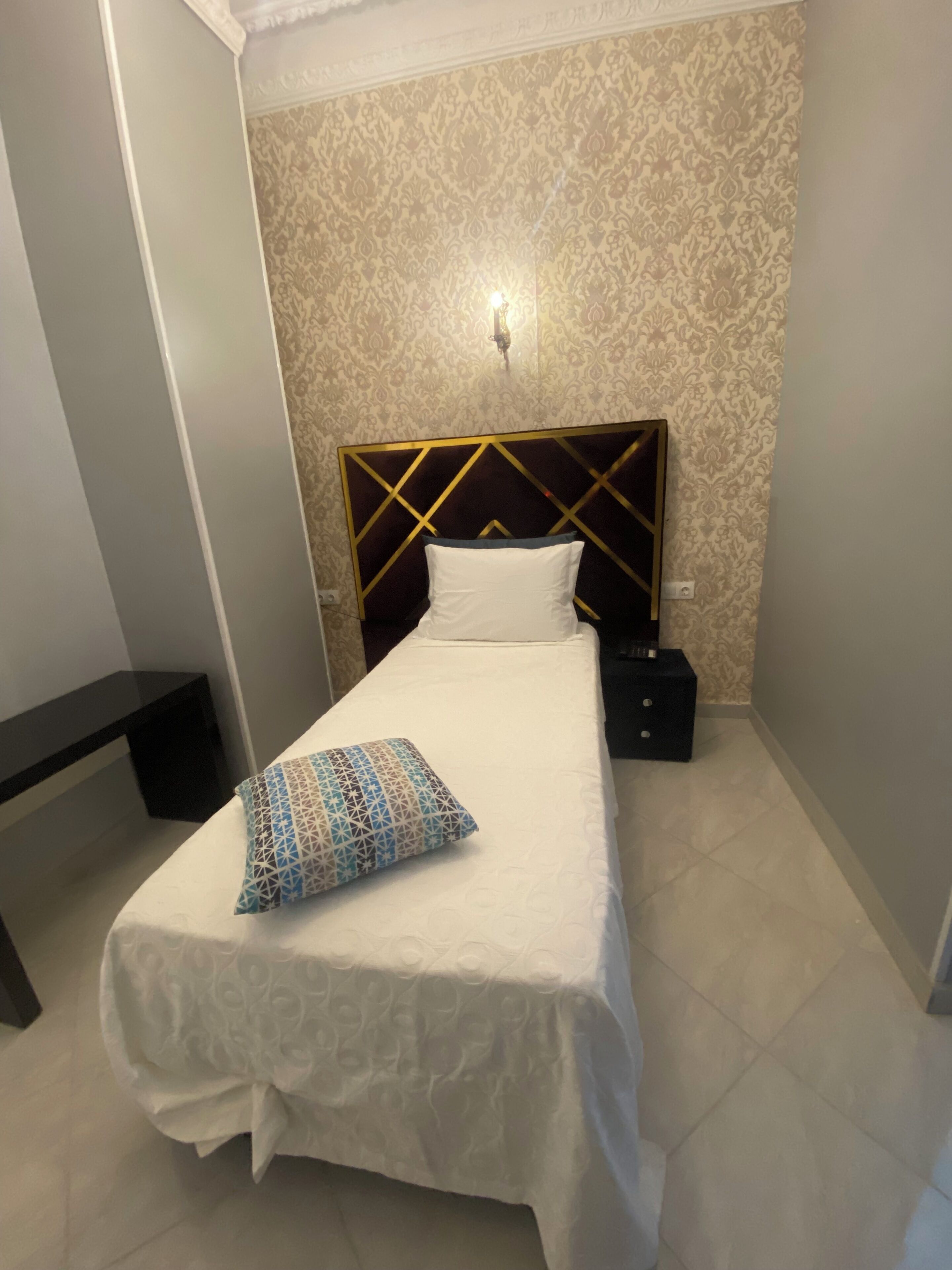 A neatly made bed with a patterned pillow, a bedside table, and a wall-mounted light fixture.