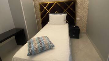 A neatly made bed with a patterned pillow, a bedside table, and a wall-mounted light fixture.
