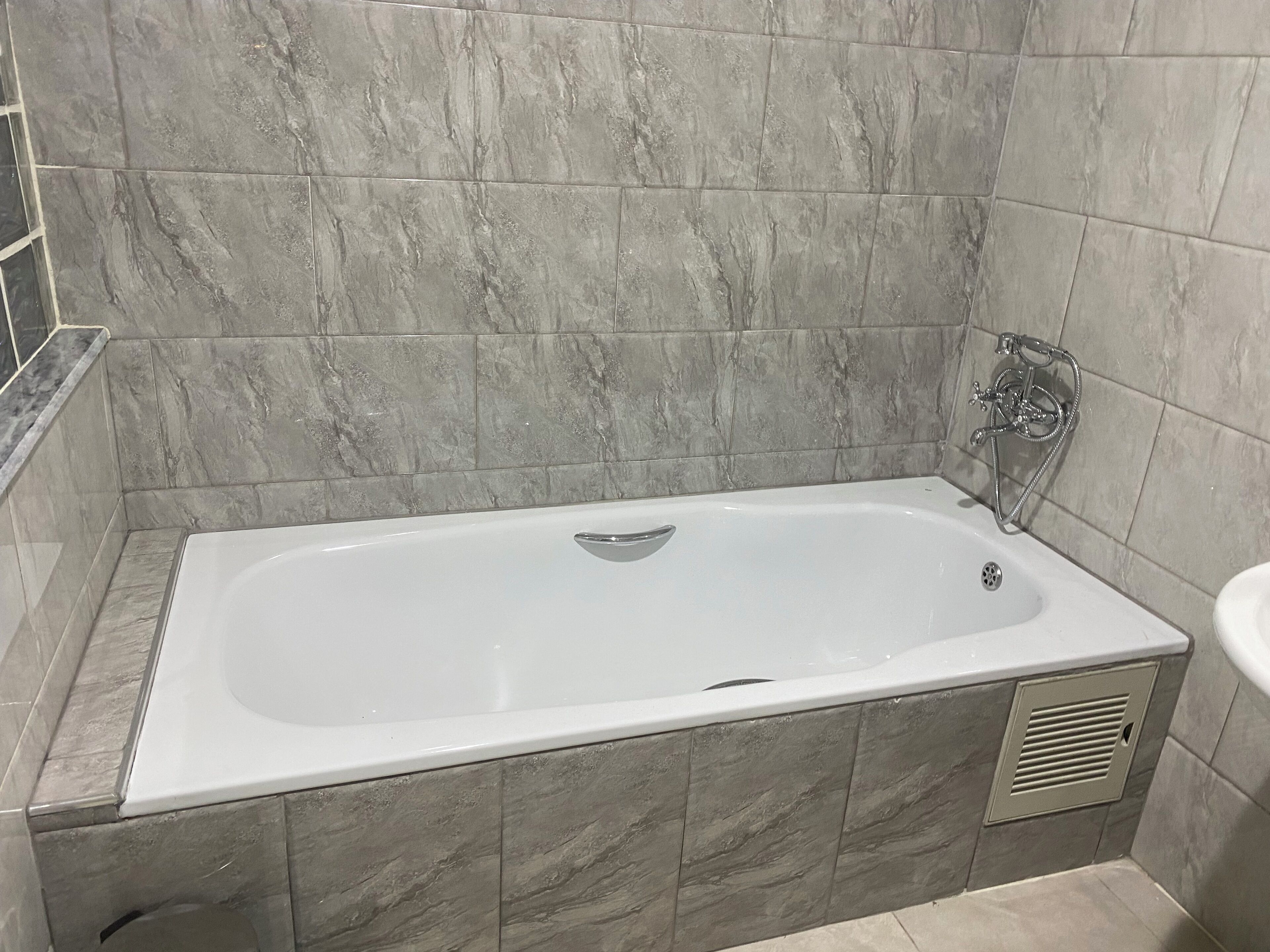 A modern bathroom with a rectangular bathtub, grey marble tiles, and a chrome faucet.