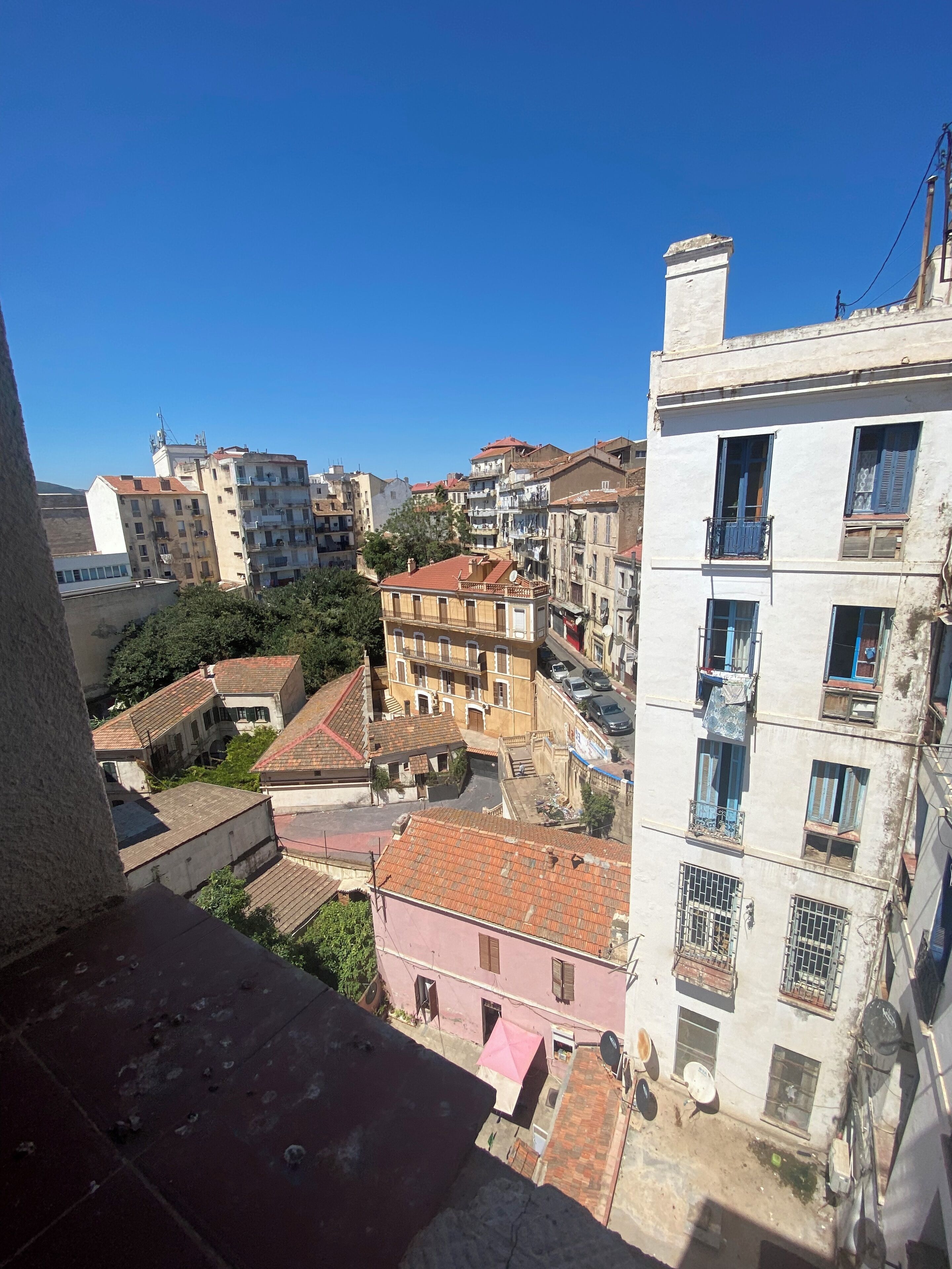 A view of a densely packed urban area with multi-story buildings, some with balconies and satellite dishes, under a clear blue sky.