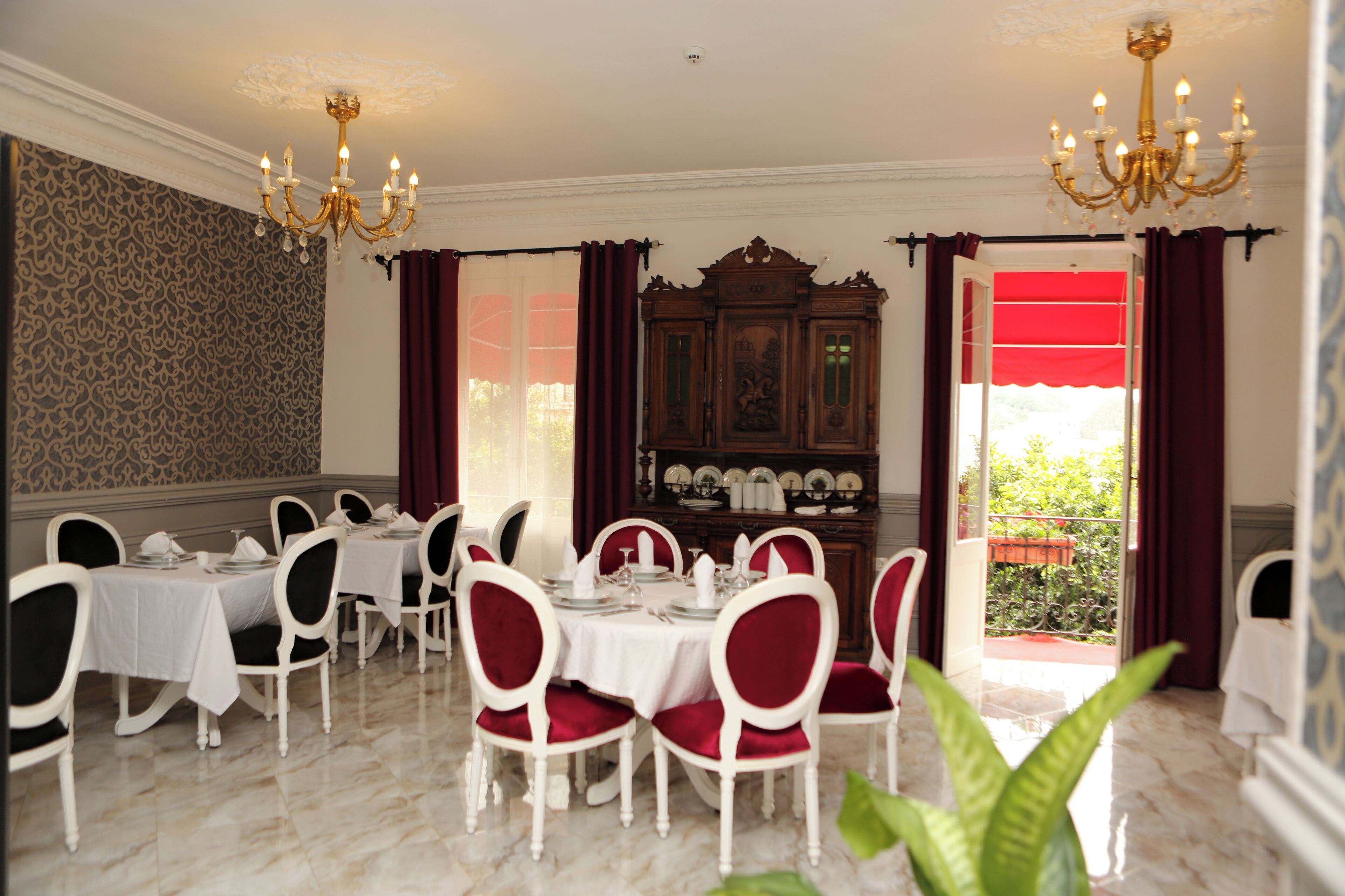 A dining area with white tables and chairs, a chandelier, and a view of the outdoors.