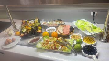 Een buffet met diverse gerechten, waaronder fruit, groenten, pasta en vlees.