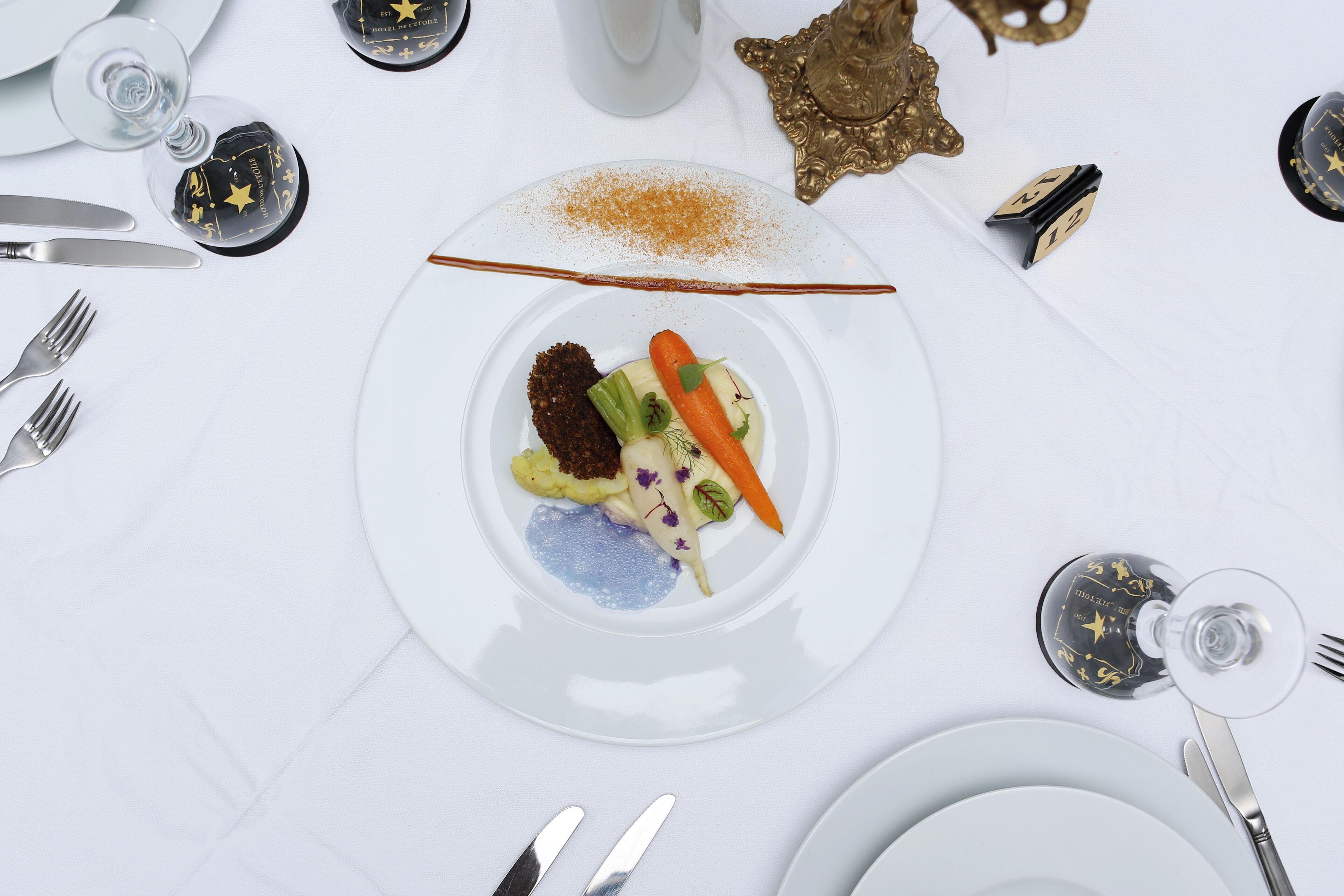A white table setting with a plate of food, silverware, and a glass of water.