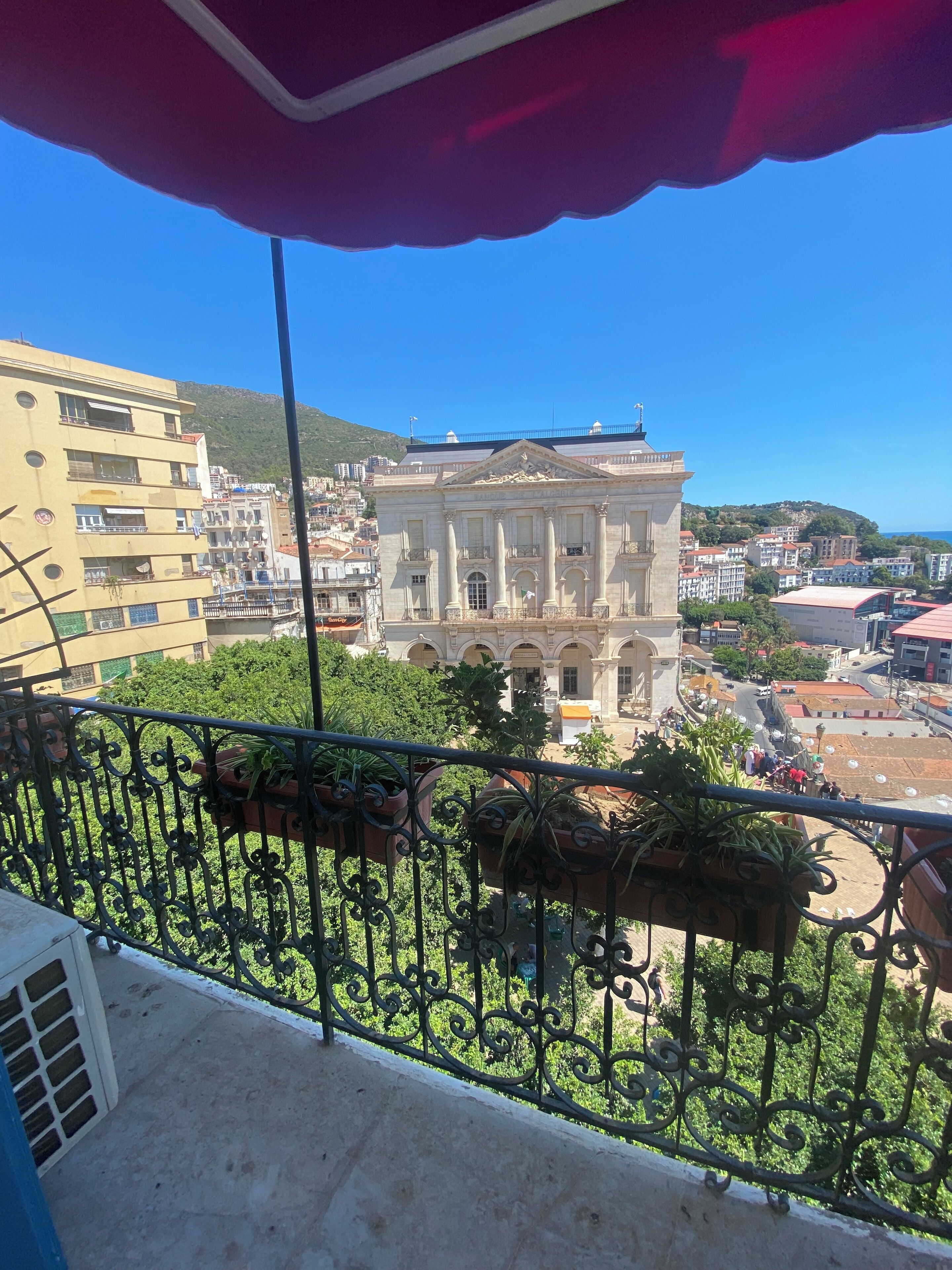 A balcony with wrought iron railings, potted plants, and a view of a historic building with classical architecture.