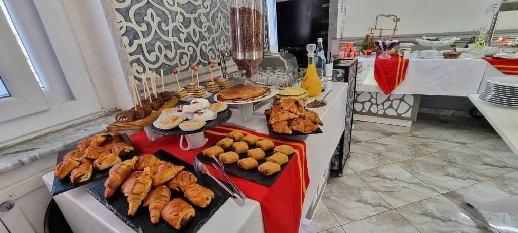 Montaje de bufé con diferentes opciones de comida, incluyendo pasteles, un dispensador de bebidas y una máquina de café.