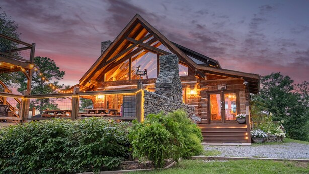 Une cabane en rondins avec une cheminée en pierre, une terrasse en bois et une enseigne sur laquelle on peut lire « Lodge ».