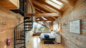 Une chambre située dans une cabane en bois, avec un escalier en colimaçon, un lit, une table de chevet et une fenêtre donnant sur un paysage agréable.