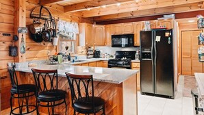A wooden cabin kitchen with a central island, bar stools, a refrigerator, a stove, and hanging pots.