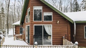 A two-story wooden cabin with a covered porch and a snow-covered roof.