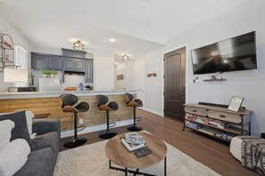 Uma sala de estar moderna com um sofá cinza, uma mesa de centro e uma TV fixada na parede.