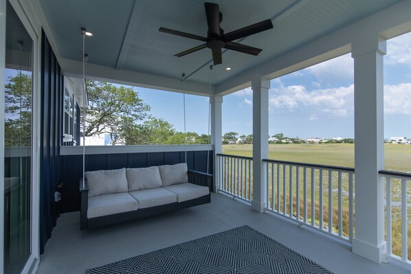 Eine überdachte Veranda mit einer Couch, Deckenventilator und Blick auf ein grünes Feld.