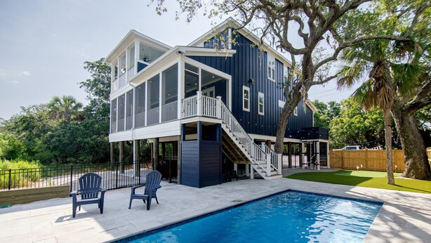 A two-story house with a pool, outdoor seating, and a staircase leading to a balcony.