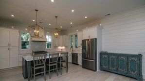 A modern kitchen with white cabinetry, a central island with chairs, a stainless steel refrigerator, and a teal painted cabinet.