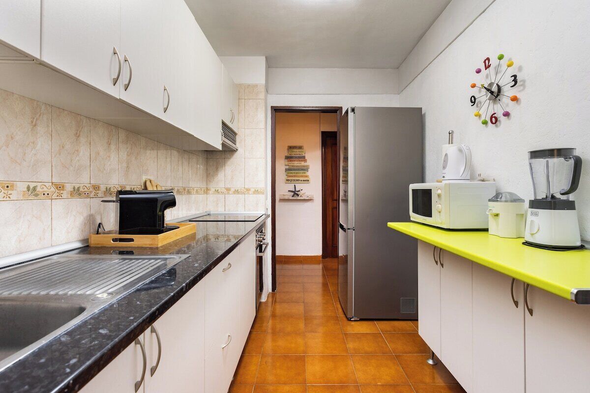 Een keuken met witte kasten, een zwart aanrecht, een magnetron, een blender en een koelkast.