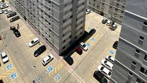 A high-rise residential building with multiple floors, a parking lot with marked handicapped spaces, and a clear blue sky with clouds. - Apartamento Park Quinet  (Juiz de Fora)