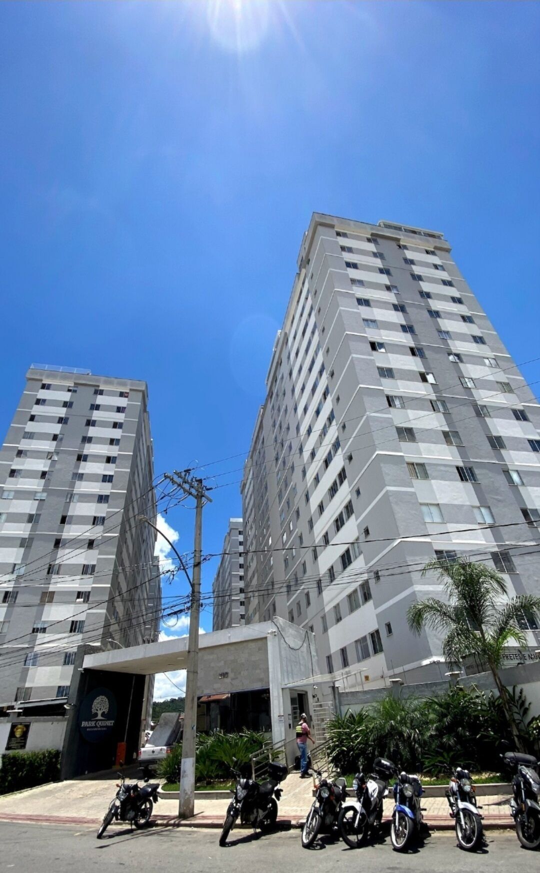 A high-rise building with multiple floors, a parking area with motorcycles, and a clear blue sky.
