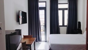 A hotel room with a bed, a desk with a chair, a TV, and two windows with curtains. - MoonStay (Ho Chi Minh City)