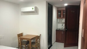 A compact room with a bed, a small dining table with chairs, a kitchenette with a sink and cabinets, and an air conditioning unit mounted on the wall. - MoonStay (Ho Chi Minh City)