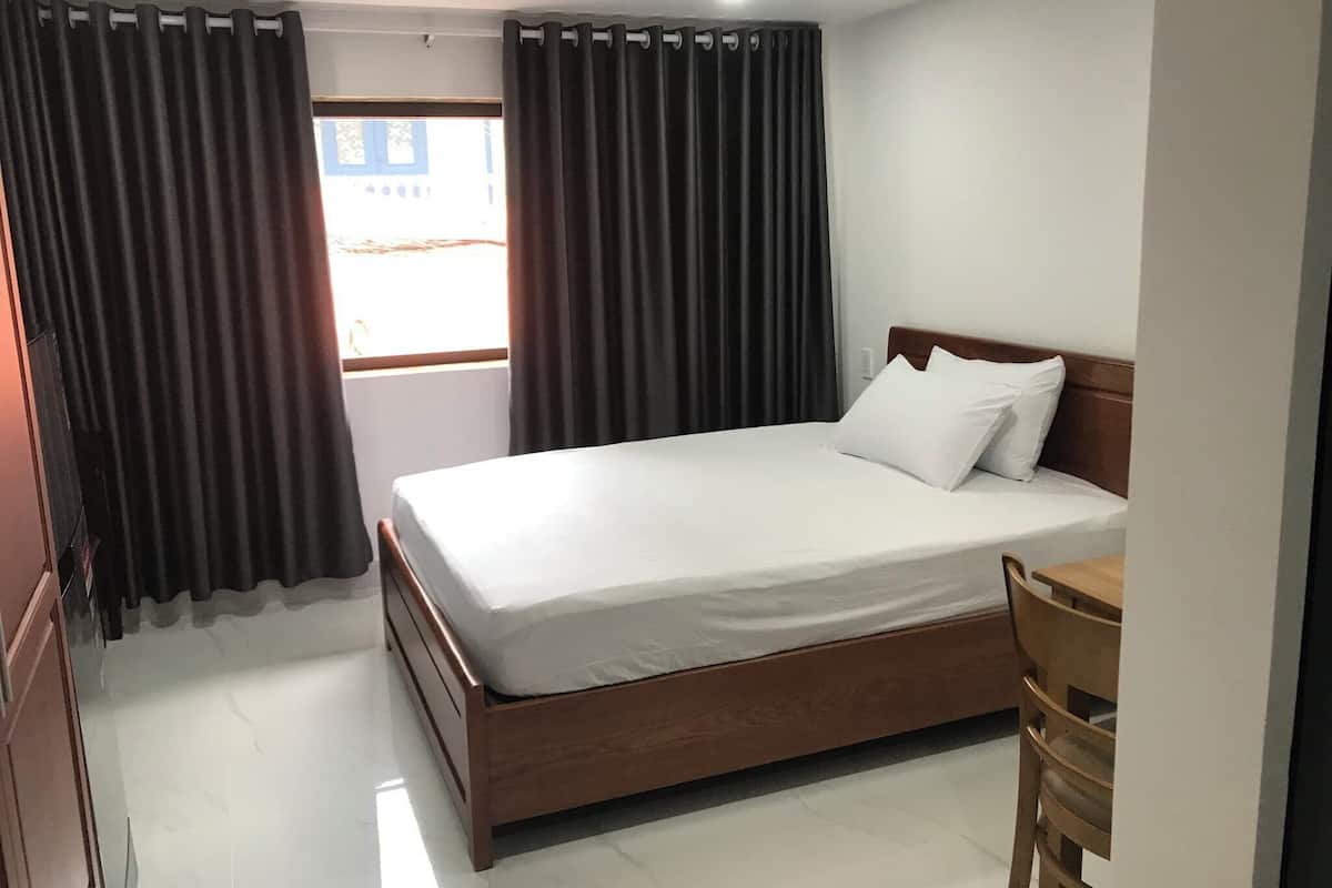 A hotel room with a wooden bed, white bedding, and a view through a window with curtains.