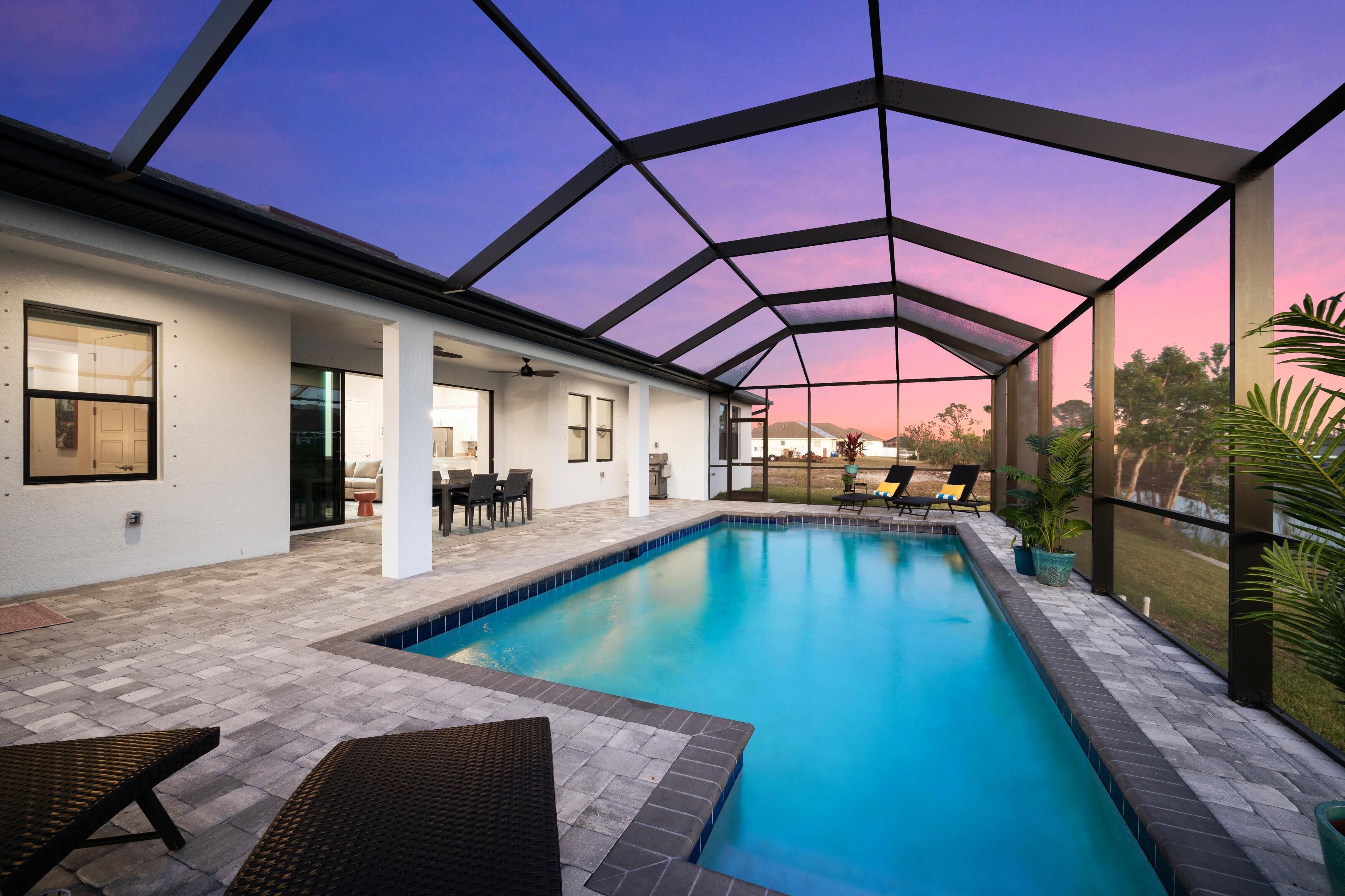 Piscina con cerramiento de vidrio, sillas de descanso y zona de patio con mobiliario exterior.