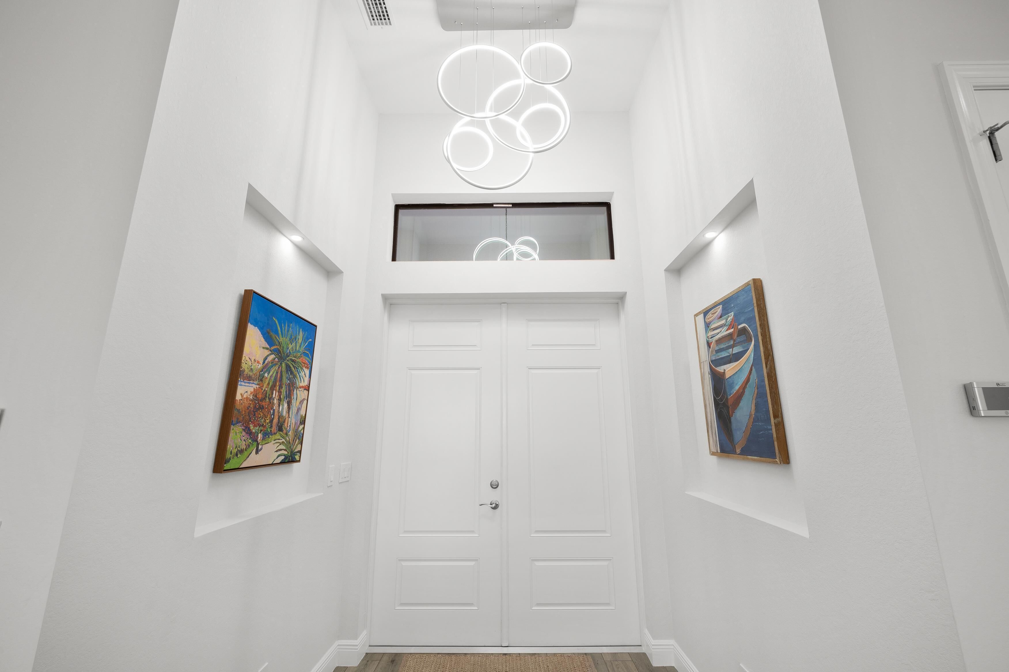 A hallway with white walls, a double door, and two paintings on either side.