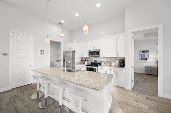 A modern kitchen with white cabinets, a granite countertop, stainless steel appliances, and pendant lighting. - Escape to Cape! 4 bed 3 bath Canal Home w/ Heated Oversized Pool & 2 King Suites (Cape Coral)