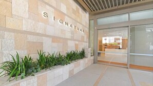 Entrada de un edificio con un letrero que dice 'SIGNATURE' y una jardinera con plantas verdes.