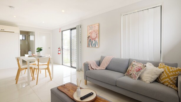Una sala de estar moderna con un sofá gris, una mesa de centro de madera y un comedor con una mesa blanca y sillas de madera.