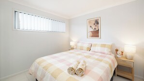 Un dormitorio con una cama, dos lámparas de noche, una mesita de noche, un cuadro enmarcado y una ventana con persianas.