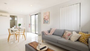 Una sala de estar moderna con un sofá gris, una mesa de centro de madera y un comedor con una mesa blanca y sillas de madera.