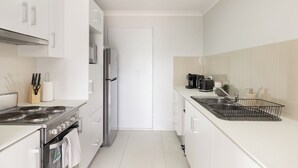 A modern kitchen with white cabinetry, a stainless steel stove, a refrigerator, and a coffee maker. - Modern Rocklea 2BR | Near Shops | Parking | 118D2 (Rocklea)