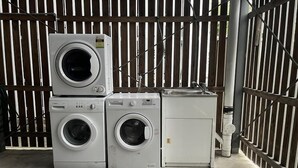 A stack of white washing machines in a garage with a wooden fence in the background. - Modern Rocklea 2BR | Near Shops | Parking | 118D2 (Rocklea)
