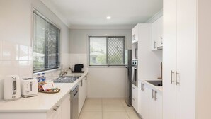 Una cocina moderna con armarios blancos, electrodomésticos de acero inoxidable y un ventanal con persianas.