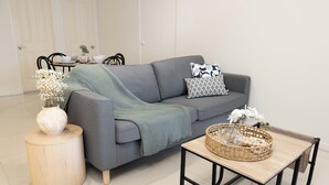 A modern living room with a grey sofa, a round wooden side table, and a coffee table with a woven basket. - Private Rocklea 1BR | Good Location | 216D1 (Rocklea)