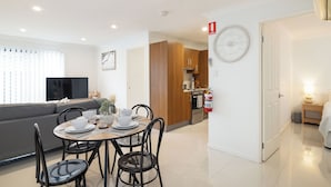 A modern living room with a sofa, TV, and dining area with chairs and a table set for four. - Private Rocklea 1BR | Good Location | 216D1 (Rocklea)