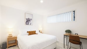 A bedroom with a bed, bedside tables with lamps, a desk with a chair, a window with blinds, and a framed picture on the wall. - Private Rocklea 1BR | Good Location | 216D1 (Rocklea)