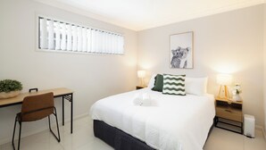 Un dormitorio ordenado con cama, mesitas de noche, un escritorio y una silla.