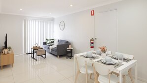 Una sala moderna con un sofá, una mesita de centro y un comedor con una mesa dispuesta para dos.