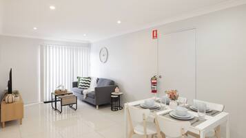 A modern living room with a sofa, a coffee table, and a dining area with a table set for two.