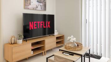 A modern living room with a large flat-screen TV displaying "NETFLIX," a wooden entertainment unit, a small table with a basket, and a chair.