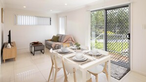 A modern living room with a dining area, a sofa, a TV, and a balcony with a metal gate.