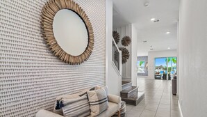 A modern living room with a patterned wall, a round mirror, a sofa with cushions, and a staircase leading to another area. - Legends Coastal Sanctuary: Private Pool, Theater, Near Disney (Kissimmee)