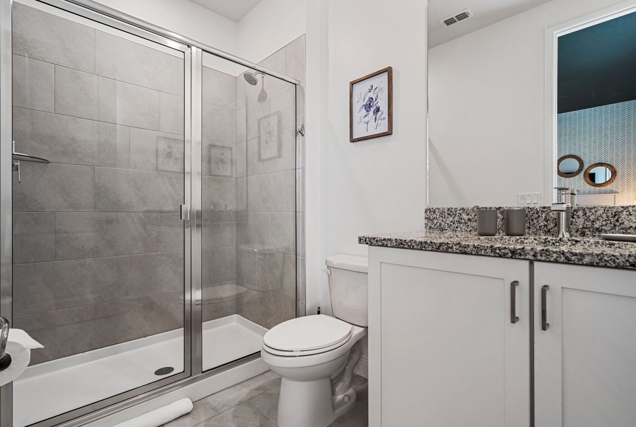 Un baño moderno con ducha de vidrio, inodoro y tocador con encimera de granito.