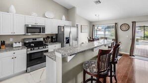 A modern kitchen with white cabinets, stainless steel appliances, and a granite countertop. - Relax & Unwind in Privacy - Heated Salt Water Pool and Spa - Villa Belle Vie (Cape Coral)