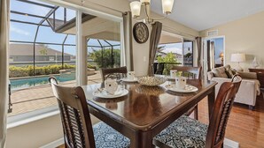 A dining area with a large table, chairs, and a chandelier. There is a view of a swimming pool and outdoor furniture. - Relax & Unwind in Privacy - Heated Salt Water Pool and Spa - Villa Belle Vie (Cape Coral)