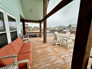 A wooden deck with a sofa and chairs, overlooking a coastal area with houses.