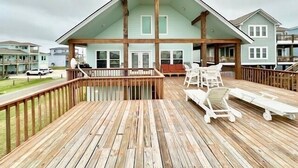 Een huis met twee verdiepingen, een houten terras, witte tuinmeubels en uitzicht op omliggende huizen.