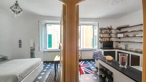 Habitación pequeña con cama, una mesita, una silla, televisor y estante con diversos objetos.